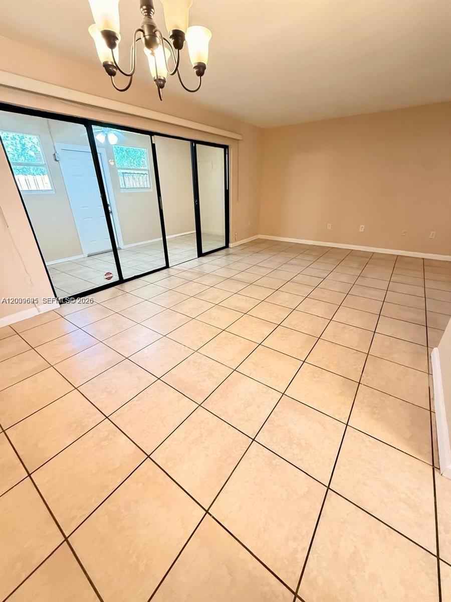 A bright, empty room features beige tile flooring, a chandelier, and sliding glass patio doors — 3301 Raleigh St # 4D, Hollywood FL 33021, HOLLYWOOD, FL
