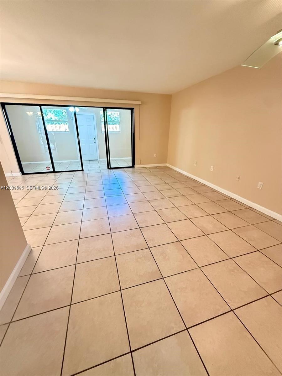 An empty room features beige tile flooring, light-colored walls, and a sliding glass door — 3301 Raleigh St # 4D, Hollywood FL 33021, HOLLYWOOD, FL