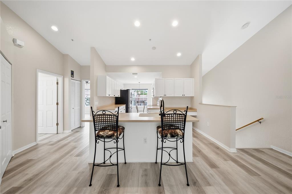 A kitchen with white cabinets, a breakfast bar with two stools, and light wood flooring — 7660 SWEETBAY CIRCLE, BRADENTON, FL