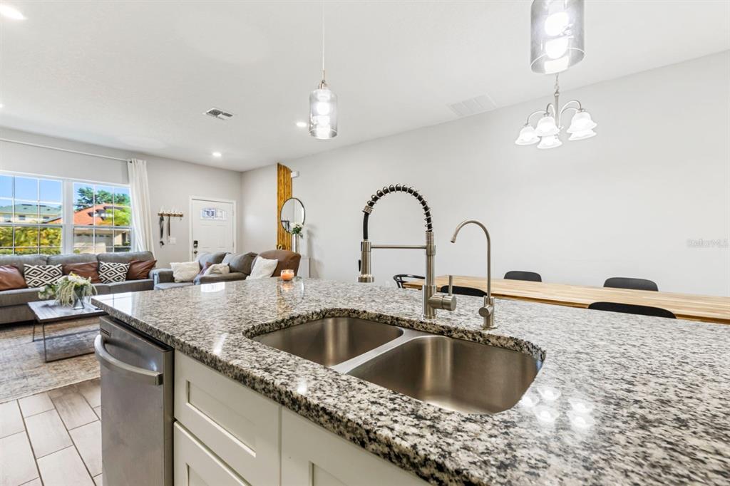 A kitchen island with a double sink and granite countertop overlooks an open-concept living area — 638 GULL DRIVE, KISSIMMEE, FL