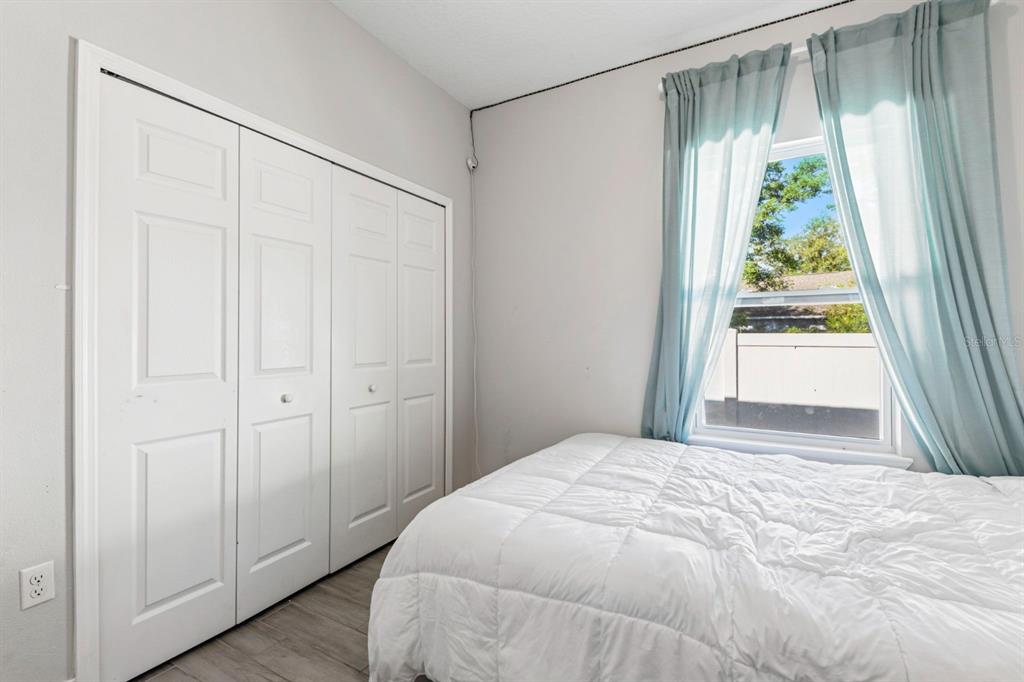 A bedroom features a white bed, light wood-look flooring, a closet, and a window with curtains — 638 GULL DRIVE, KISSIMMEE, FL