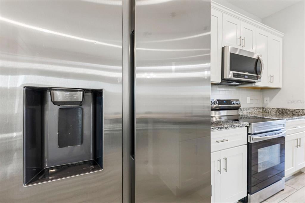 A stainless steel refrigerator stands beside a kitchen with white cabinets and granite countertops — 638 GULL DRIVE, KISSIMMEE, FL