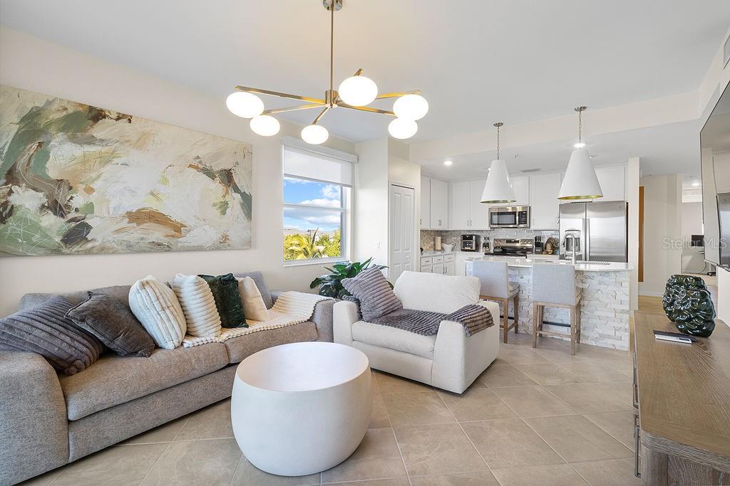 A living room with a sofa, armchair, coffee table, and an open kitchen with bar seating — 5583 DOUBLE EAGLE CIRCLE UNIT 4128, AVE MARIA, FL