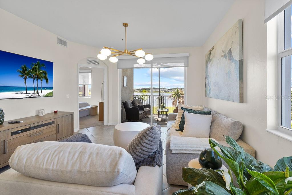 A living room features a sofa, television, modern chandelier, and a balcony overlooking a lake — 5583 DOUBLE EAGLE CIRCLE UNIT 4128, AVE MARIA, FL
