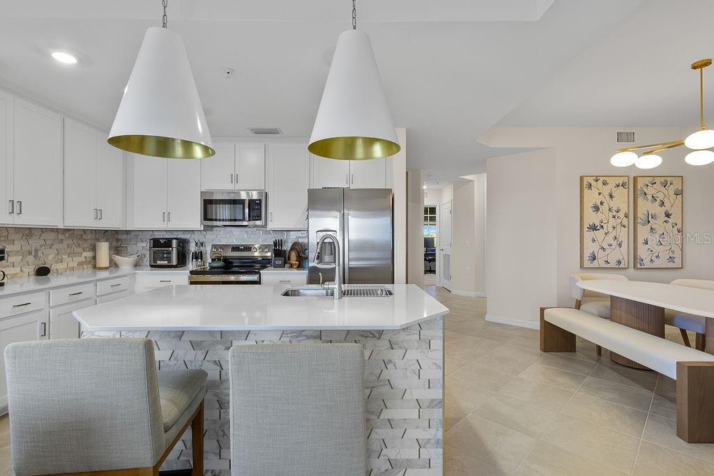 A modern kitchen features white cabinetry, a marble-tiled island, and an adjacent dining area — 5583 DOUBLE EAGLE CIRCLE UNIT 4128, AVE MARIA, FL