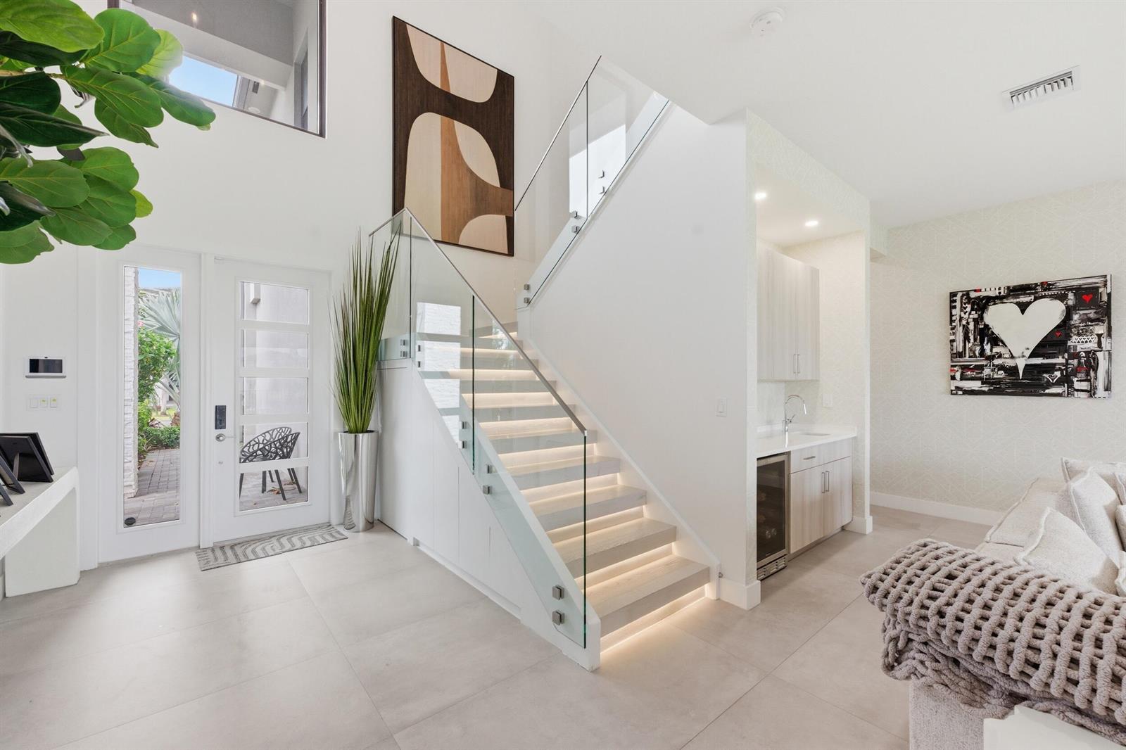 A modern entryway features a glass-railed staircase with illuminated steps and an adjacent wet bar — 8568 Crystal Downs Avenue, Boca Raton FL 33434, BOCA RATON, FL