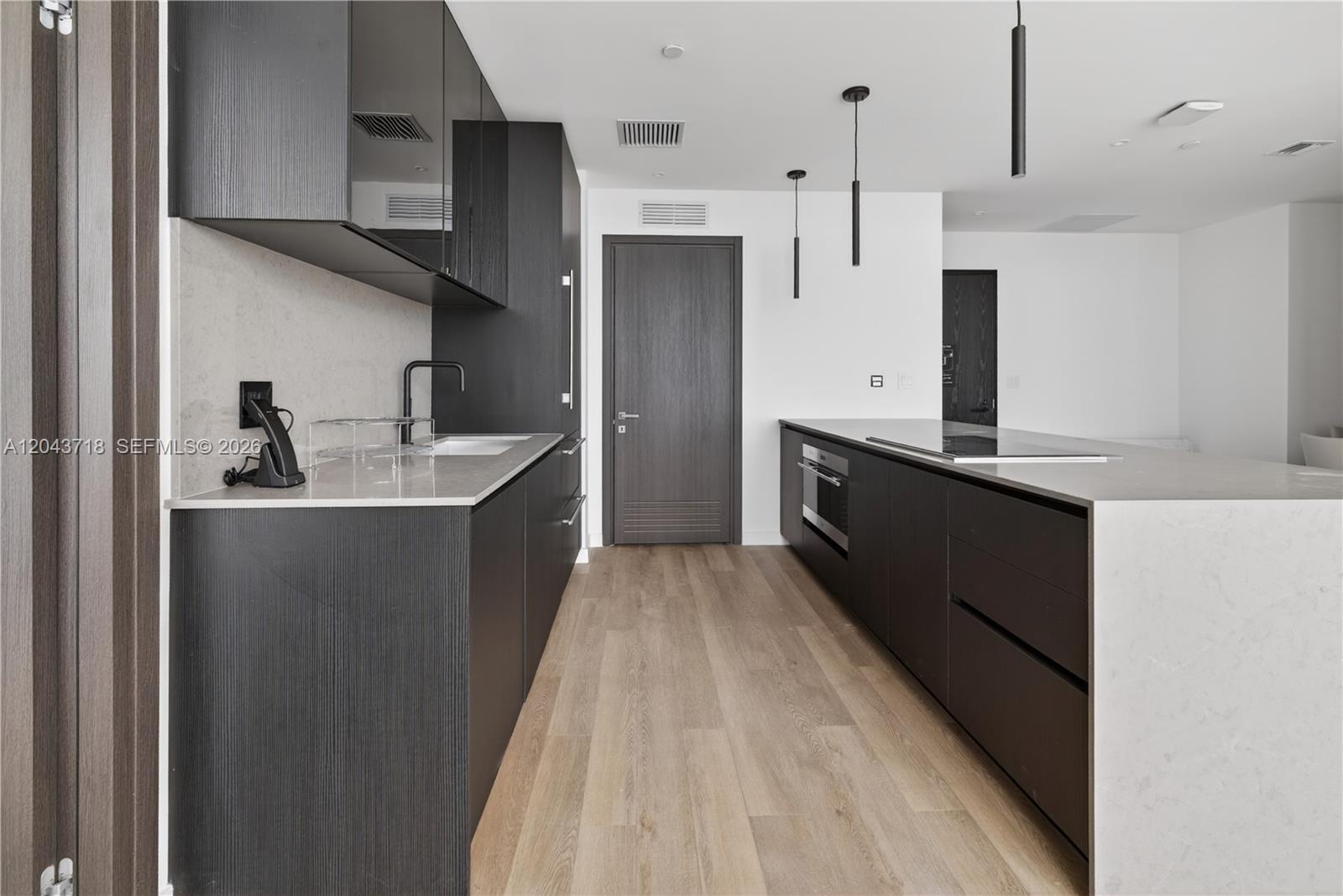 A modern kitchen features dark wood cabinetry, light stone countertops, and a central island — 20 NE 11th # 4701, Miami FL 33132, MIAMI, FL