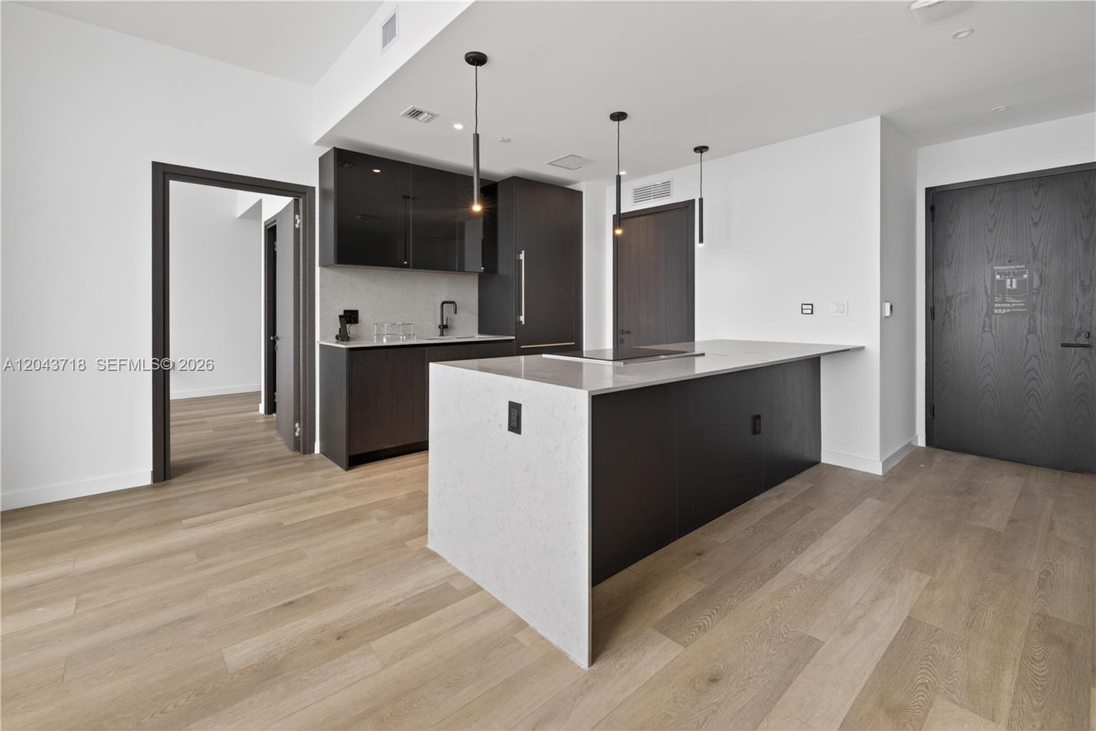 A modern kitchen features dark cabinetry, a stone-topped island, and light wood flooring — 20 NE 11th # 4701, Miami FL 33132, MIAMI, FL