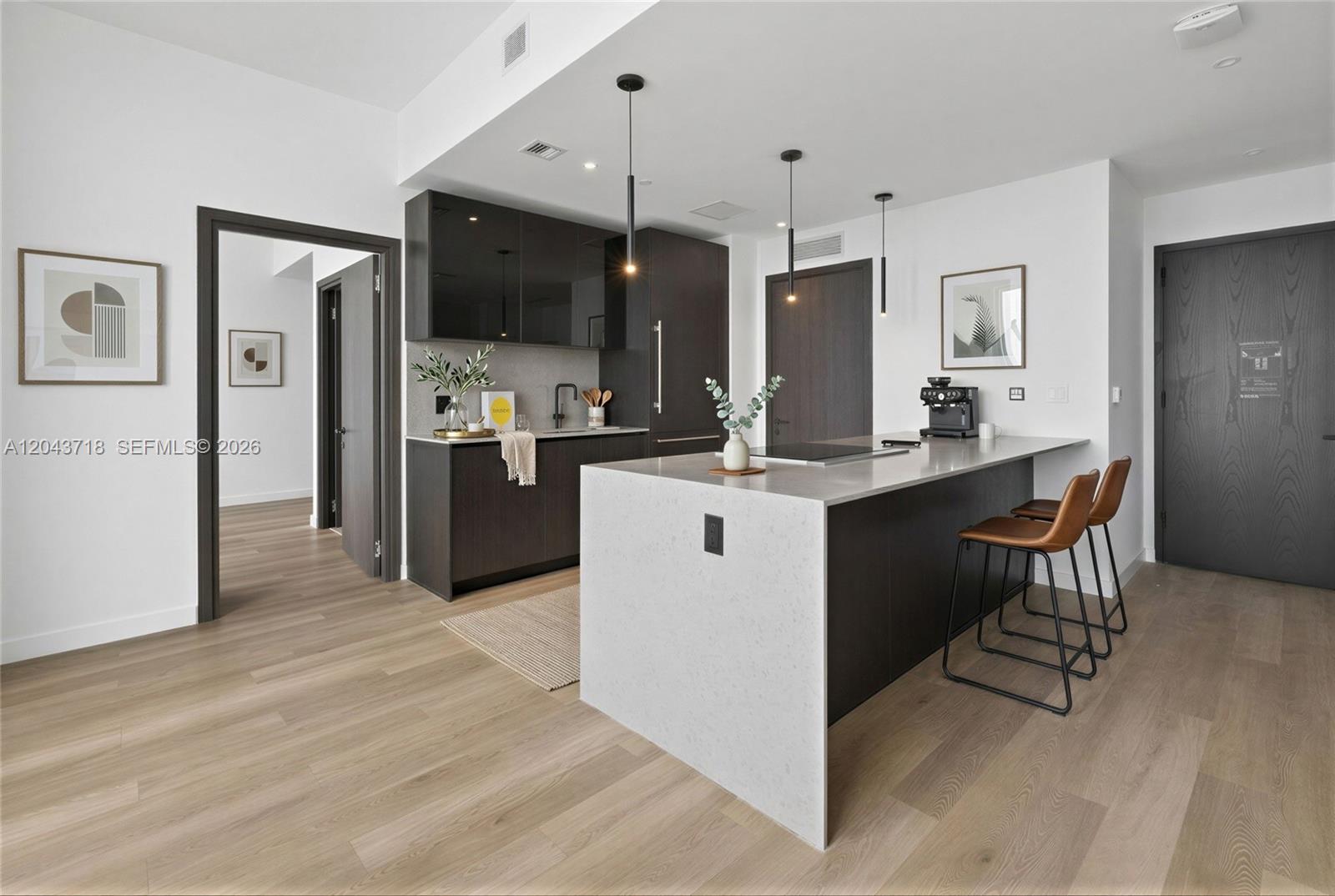 A modern kitchen features dark cabinetry, a quartz waterfall island, and light wood flooring — 20 NE 11th # 4701, Miami FL 33132, MIAMI, FL