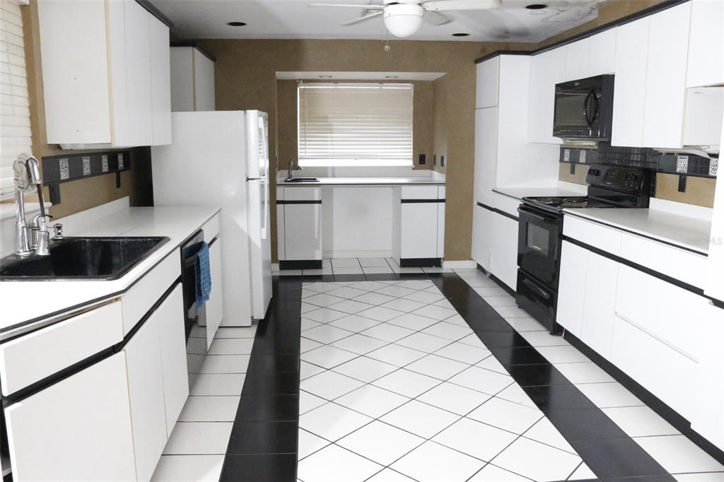 A kitchen features white cabinets, black appliances, and a floor with white and black tiles — 655 PINECREST DRIVE, BARTOW, FL