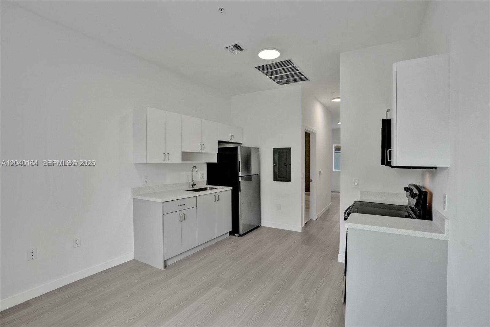 A minimalist kitchen features white cabinets, stainless steel appliances, and light wood-look flooring — 1567 NW 1st St # 5, Miami FL 33125, MIAMI, FL