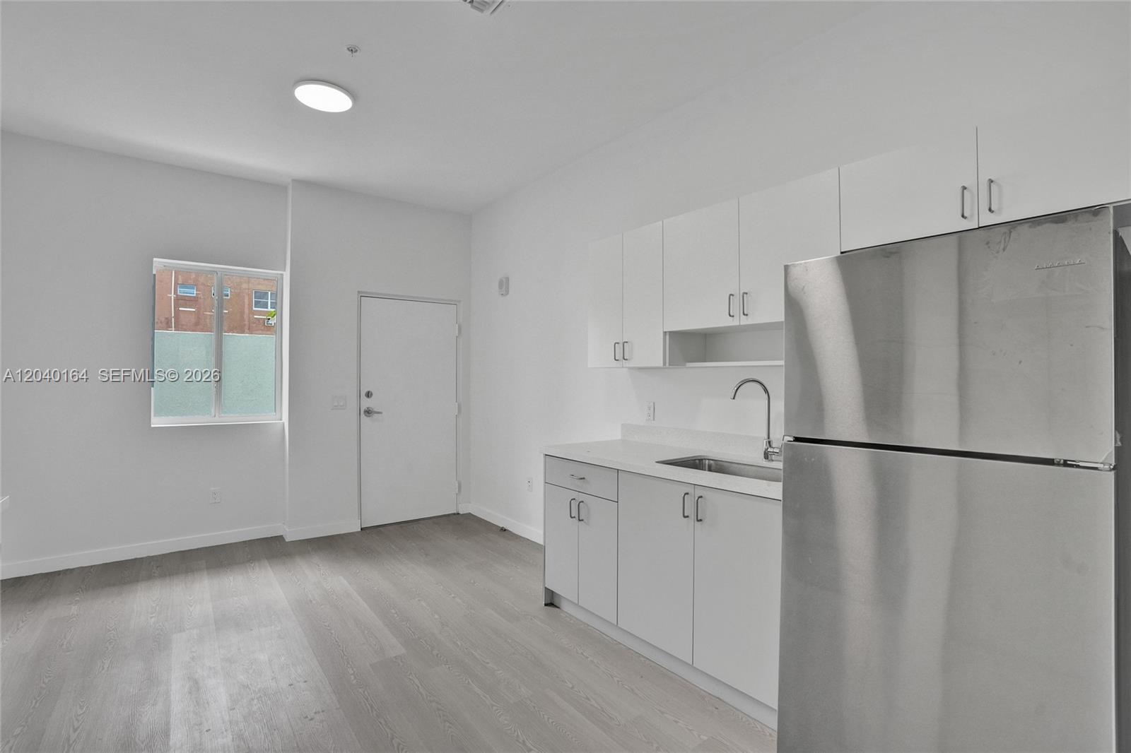 A minimalist kitchen features white cabinets, stainless steel appliances, and light wood-look flooring — 1567 NW 1st St # 5, Miami FL 33125, MIAMI, FL