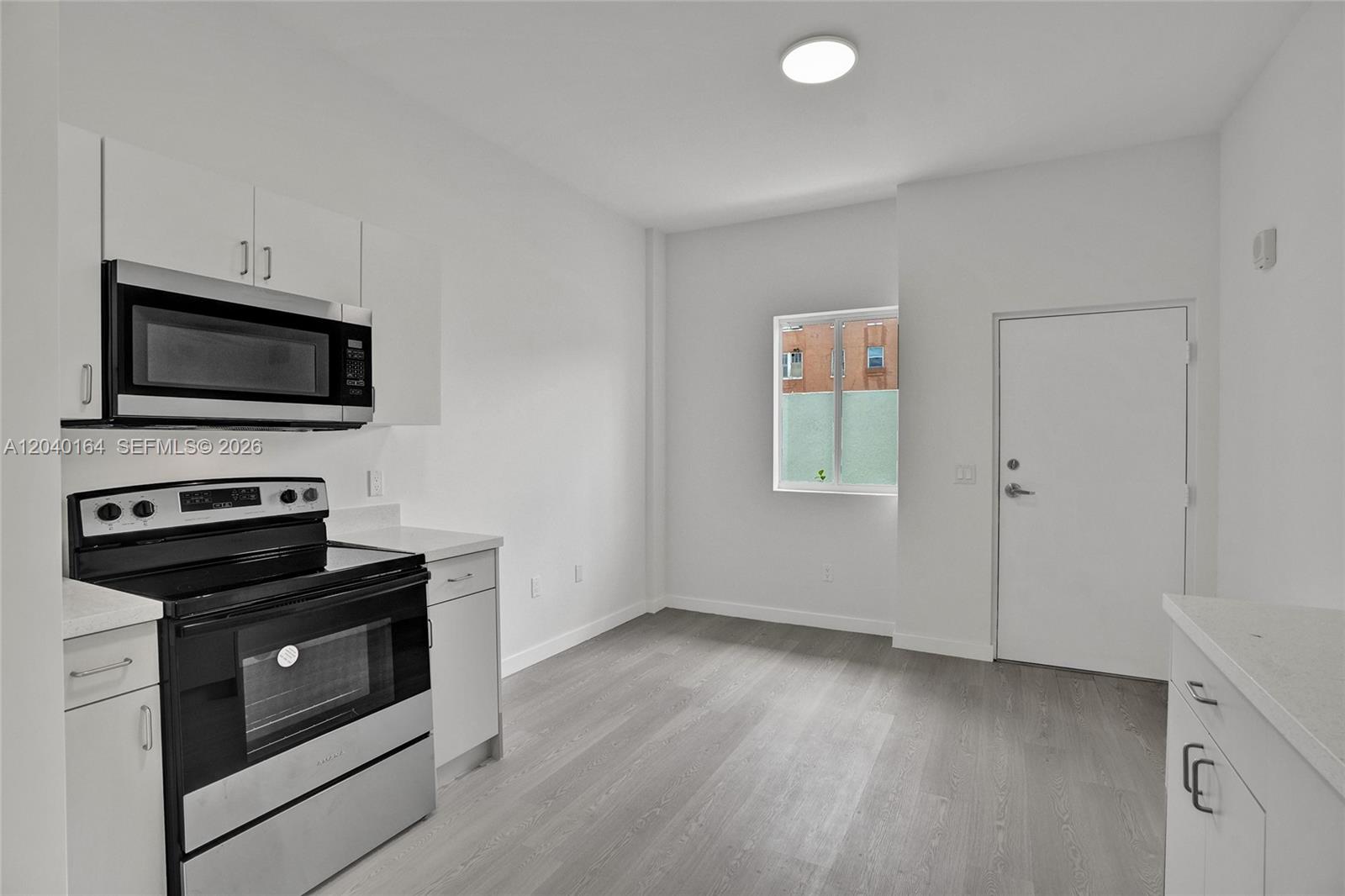 A white kitchen features stainless steel appliances, light wood-look flooring, and a single window — 1567 NW 1st St # 5, Miami FL 33125, MIAMI, FL