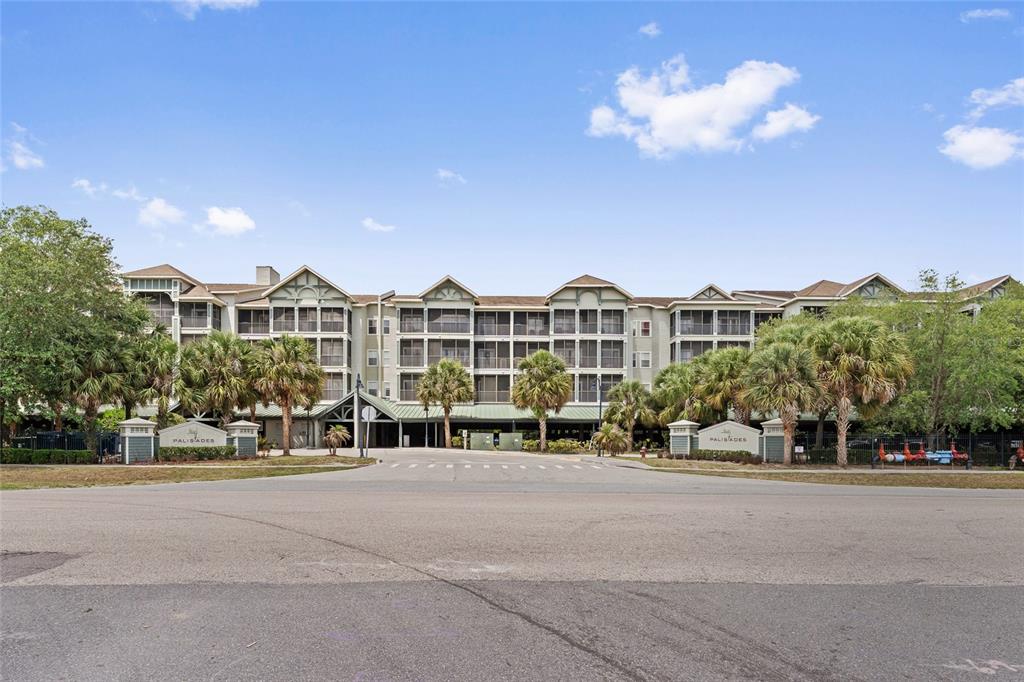 A multi-story apartment complex with screened balconies and palm trees sits behind a paved entrance — 14200 AVALON ROAD UNIT 409, WINTER GARDEN, FL