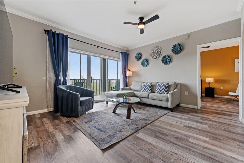 A living room features a gray sectional, blue armchair, area rug, and a balcony view — 14200 AVALON ROAD UNIT 409, WINTER GARDEN, FL