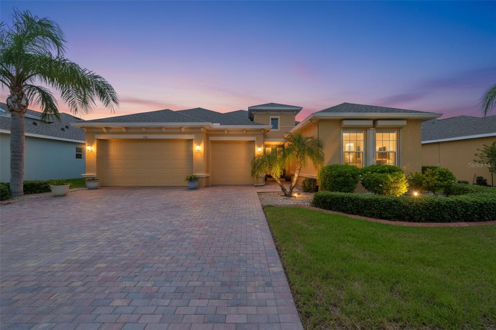 A single-story house with a paved driveway, three-car garage, and landscaped front yard at dusk — 1719 PACIFIC DUNES DR, SUN CITY CENTER, FL