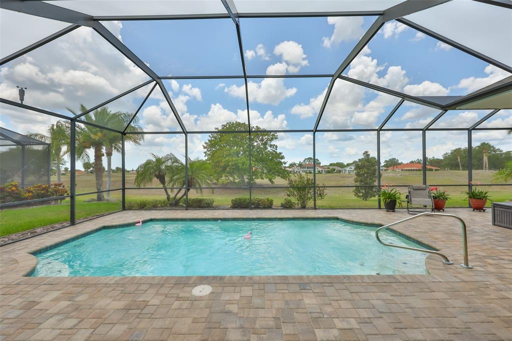 A screened-in swimming pool with a paver deck overlooks a grassy field and palm trees — 1719 PACIFIC DUNES DR, SUN CITY CENTER, FL