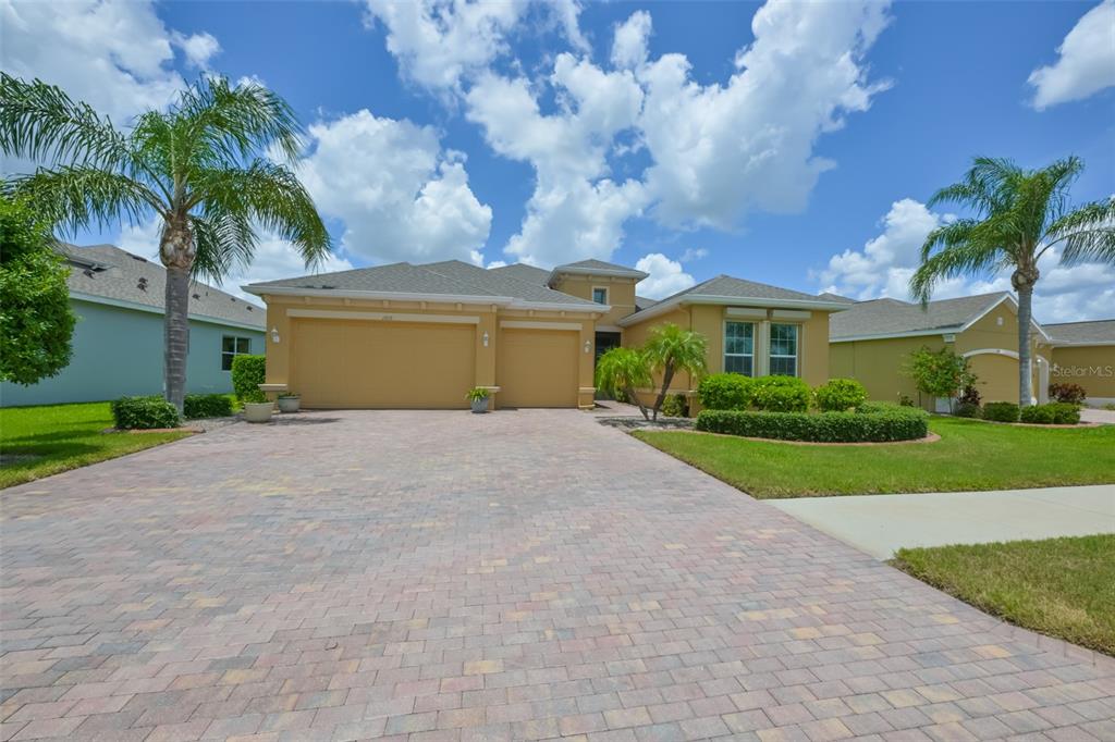 A yellow single-story house features a paved driveway, a three-car garage, and two palm trees — 1719 PACIFIC DUNES DR, SUN CITY CENTER, FL