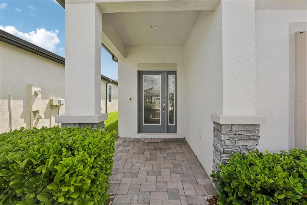 A paved walkway leads to a front entrance with a decorative glass door and stone-accented columns — 7114 GULF CYPRESS AVENUE, LAND O LAKES, FL