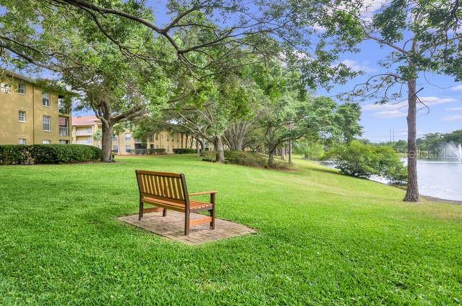 A wooden bench sits on a brick pad in a grassy park beside a lake — 2690 CORAL LANDINGS BOULEVARD UNIT 438, PALM HARBOR, FL