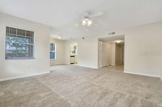 A carpeted living room features a ceiling fan, a window with blinds, and an open kitchen — 2690 CORAL LANDINGS BOULEVARD UNIT 438, PALM HARBOR, FL