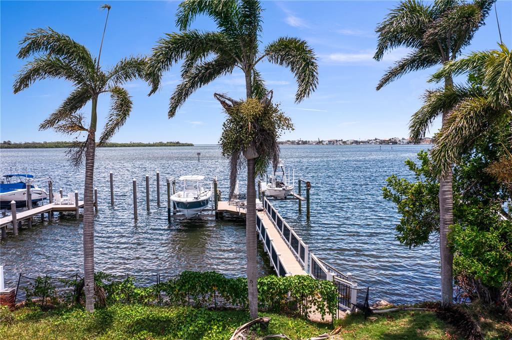 A wooden dock with two boats extends into a bay framed by palm trees — 6527 BAYOU GRANDE BLVD NE, ST PETERSBURG, FL