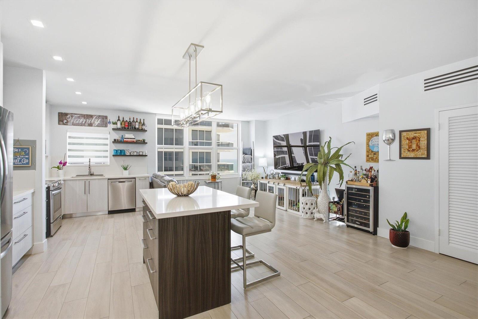 A modern kitchen and living area features a central island, stainless appliances, and light flooring — 4747 Collins Avenue # 1109, Miami Beach FL 33140, MIAMI BEACH, FL