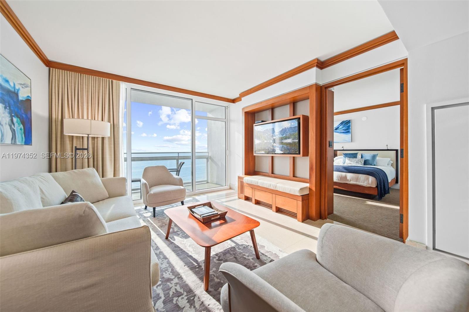 A living room with a wooden media unit, beige furniture, and a view of the ocean — 6801 Collins Ave # 604, Miami Beach FL 33141, MIAMI BEACH, FL