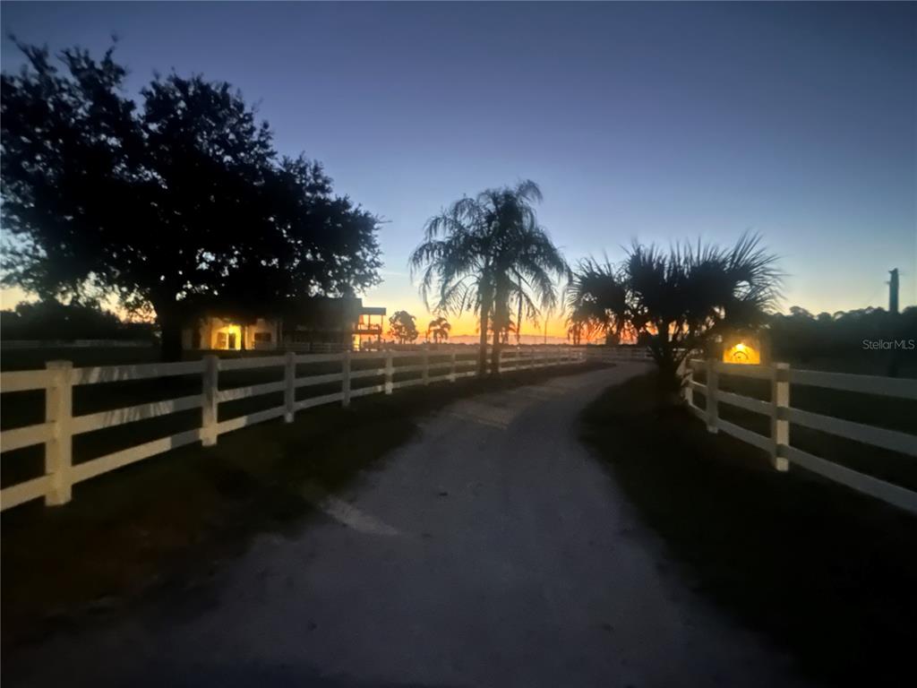 A dirt driveway leads toward a house at sunset, framed by white split-rail fencing — 664 S LAKE STARR BOULEVARD, LAKE WALES, FL