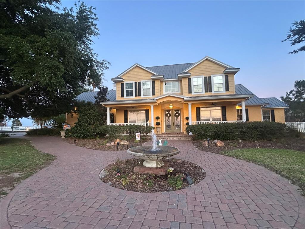A two-story yellow house with a metal roof, front porch, and a circular fountain — 664 S LAKE STARR BOULEVARD, LAKE WALES, FL