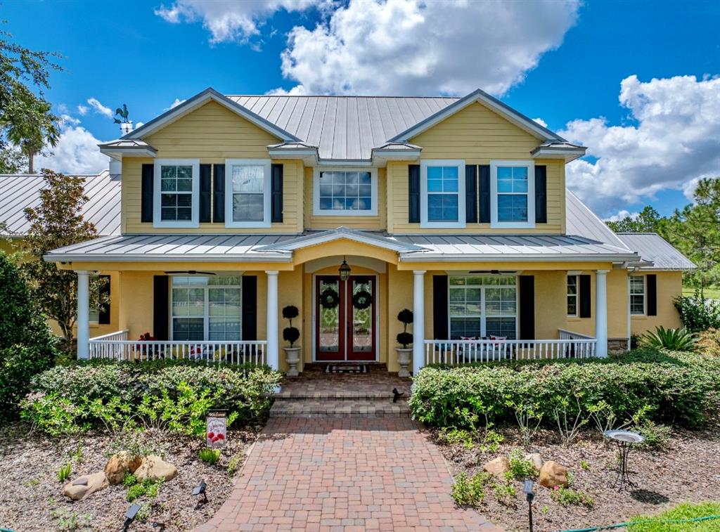A two-story yellow house with a metal roof and a brick walkway leading to the entrance — 664 S LAKE STARR BOULEVARD, LAKE WALES, FL
