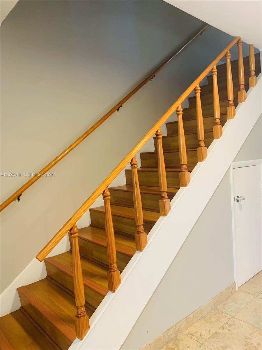 A wooden staircase with a matching handrail and balusters ascends along a light-colored wall — 1651 NE 115th St # 21C, Miami FL 33181, MIAMI, FL