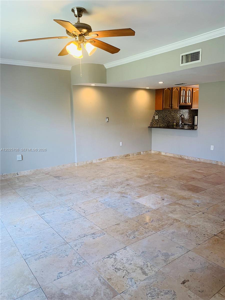 An open-concept living area features large stone floor tiles, a ceiling fan, and a kitchen pass-through — 1651 NE 115th St # 21C, Miami FL 33181, MIAMI, FL