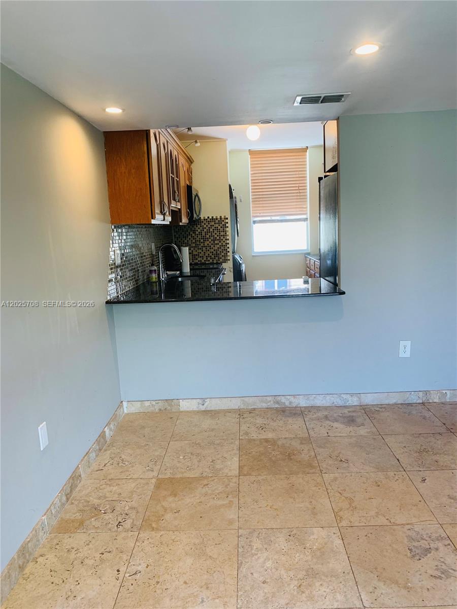 A kitchen with wood cabinets and a black countertop overlooks a tiled dining area — 1651 NE 115th St # 21C, Miami FL 33181, MIAMI, FL