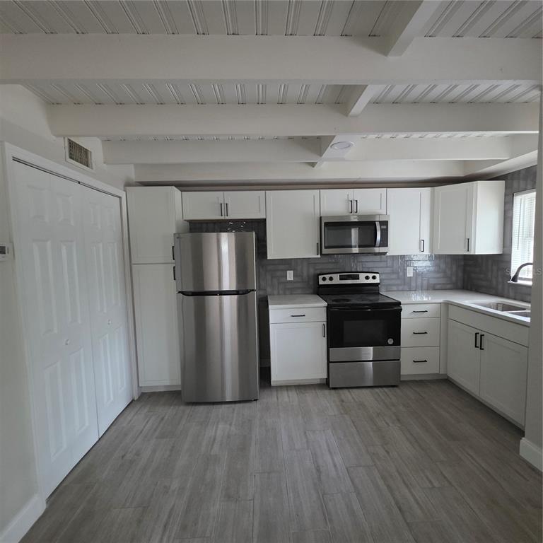 A kitchen with white cabinets, stainless steel appliances, gray tile backsplash, and wood-look flooring — 5101 ORANGE AVENUE N UNIT B, WINTER PARK, FL