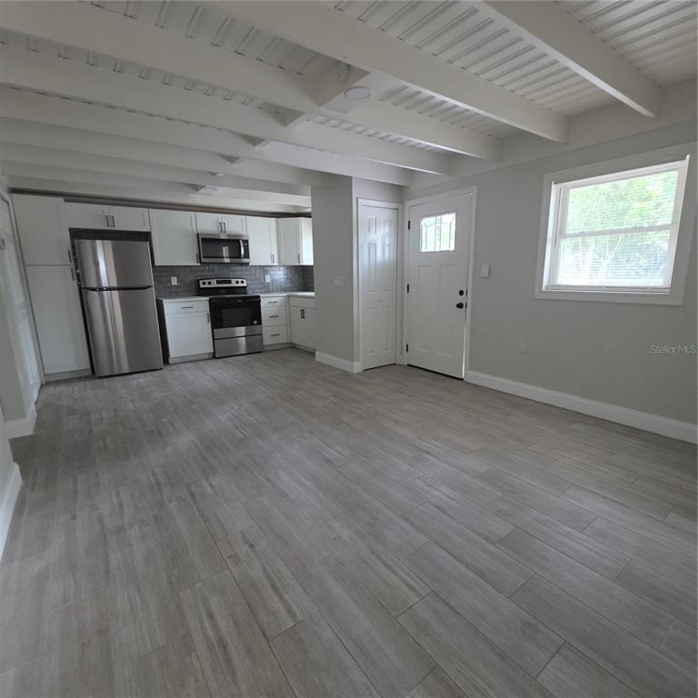A kitchen with white cabinets and stainless steel appliances opens into a room with wood-look flooring — 5101 ORANGE AVENUE N UNIT B, WINTER PARK, FL