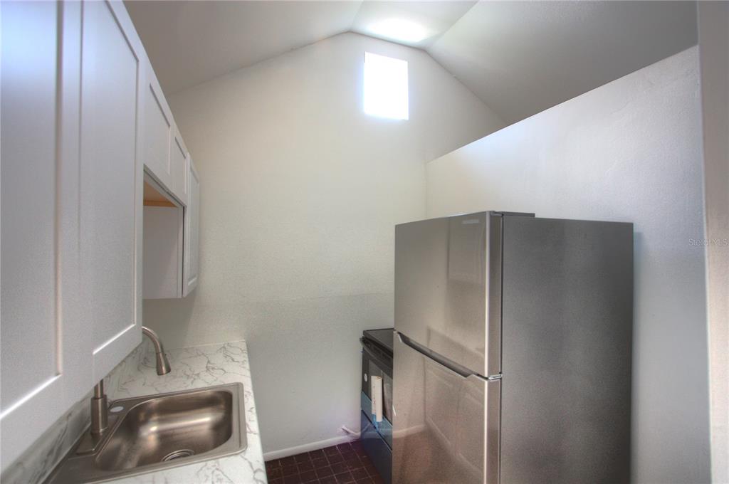 A small kitchen features white cabinets, a marble-patterned countertop, a stainless steel sink, and refrigerator — 301 S OSPREY AVENUE, SARASOTA, FL