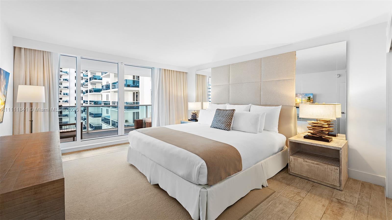 A modern bedroom features a king bed, upholstered headboard, mirrored walls, and a private balcony — 102 24th St # 904, Miami Beach FL 33139, MIAMI BEACH, FL