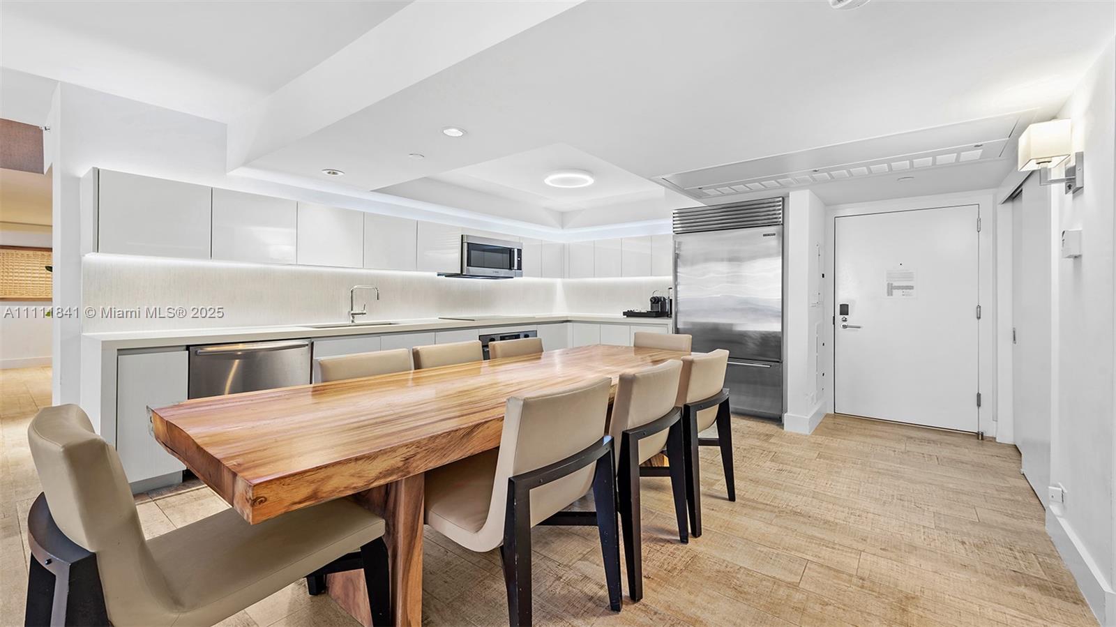 A modern kitchen features white cabinetry, stainless steel appliances, and a large wooden dining table — 102 24th St # 904, Miami Beach FL 33139, MIAMI BEACH, FL