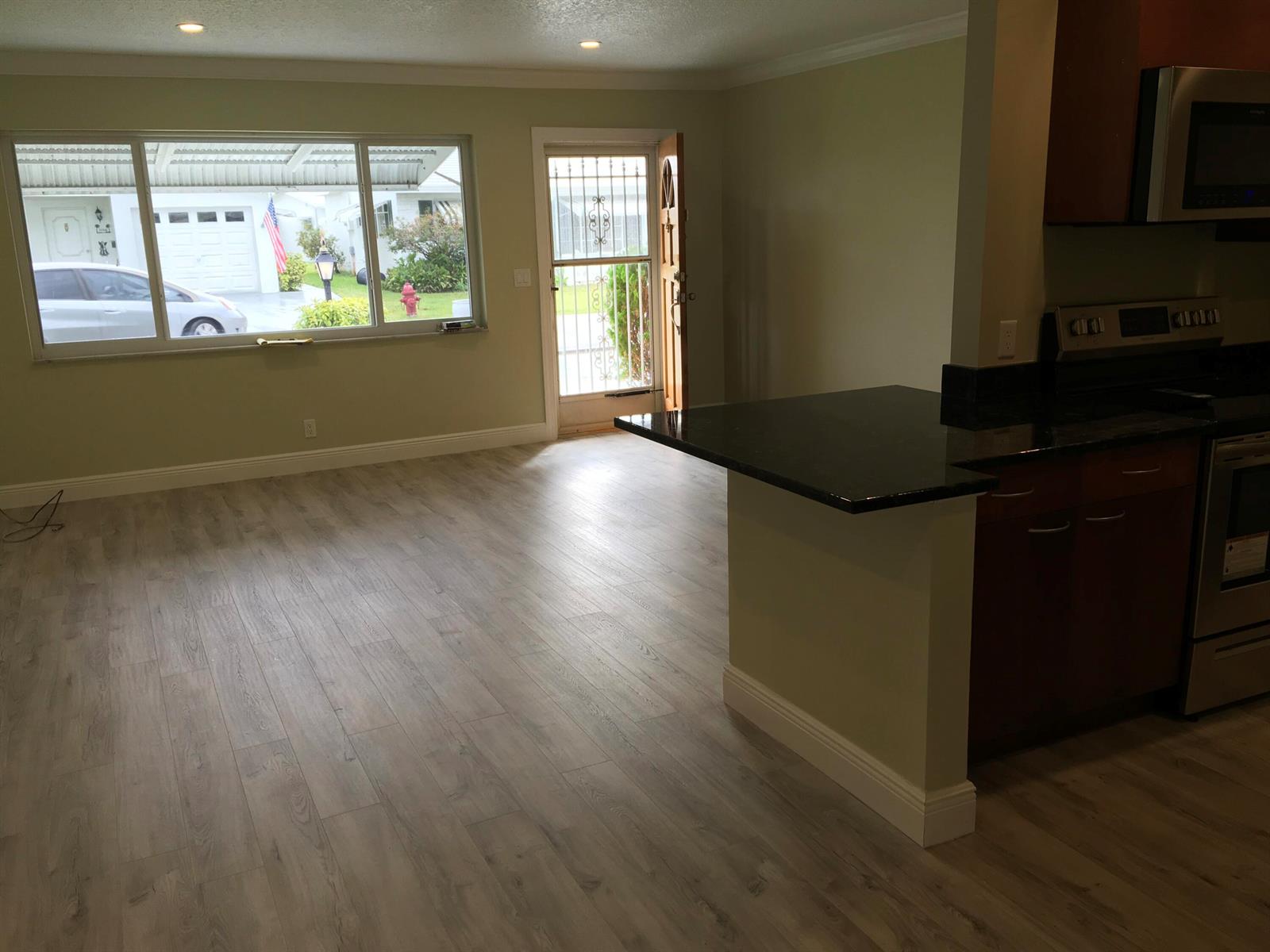 An open-concept living area features light wood-look flooring, a kitchen peninsula, and a large window — 1101 Leisure Lane, Boynton Beach FL 33426, BOYNTON BEACH, FL