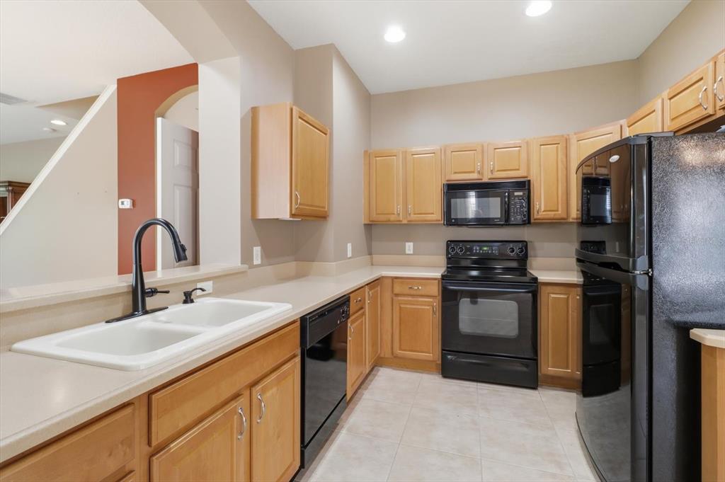 A kitchen features light wood cabinets, black appliances, beige countertops, and a double-basin sink — 1668 W SPRING MEADOW LOOP, LECANTO, FL