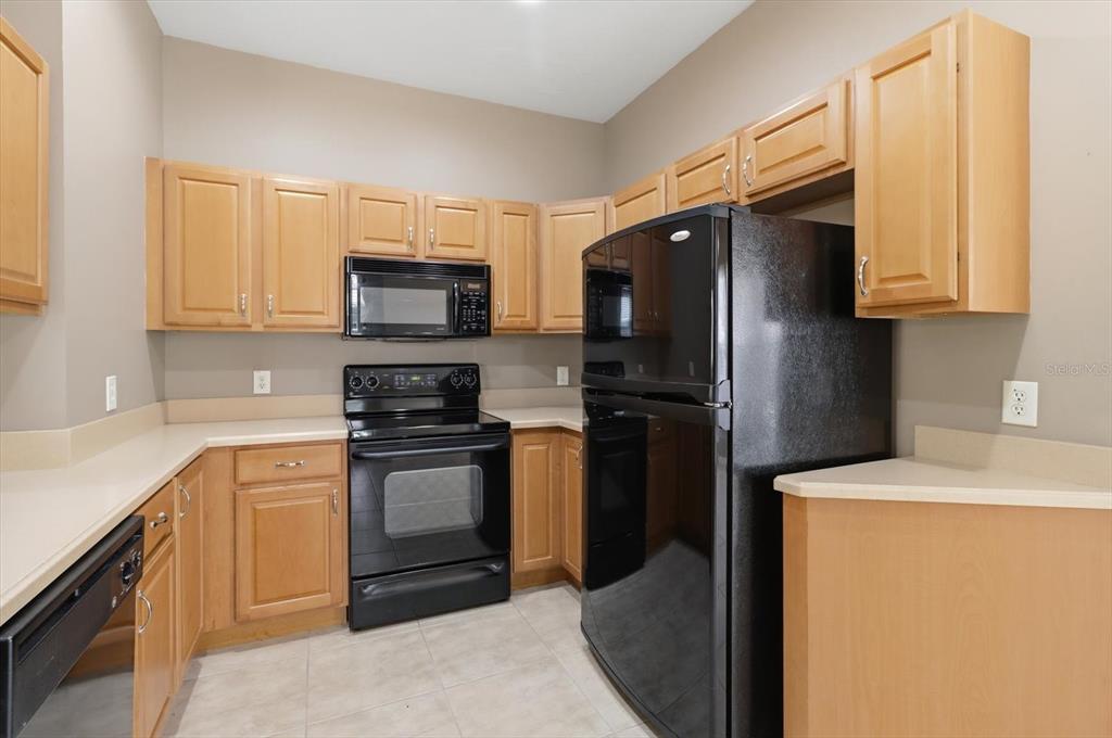 A kitchen features light wood cabinets, black appliances, beige countertops, and light tile flooring — 1668 W SPRING MEADOW LOOP, LECANTO, FL