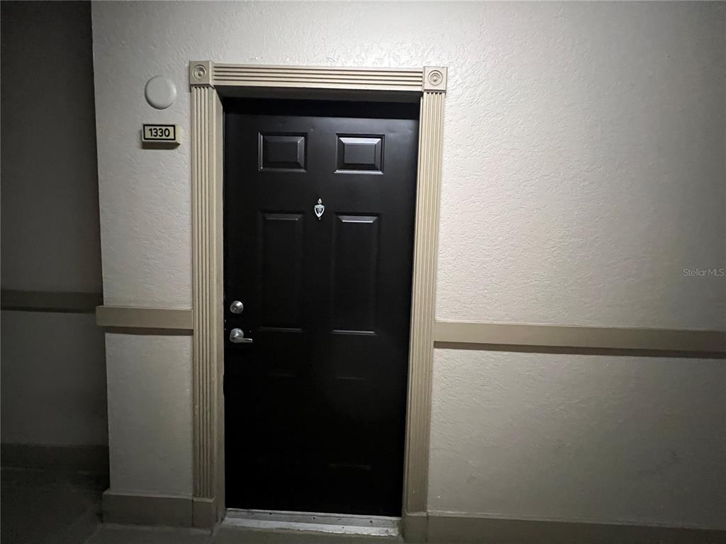 A black front door with a number plate labeled 1330 is set in a beige wall — 501 KNIGHTS RUN AVENUE UNIT 1330, TAMPA, FL