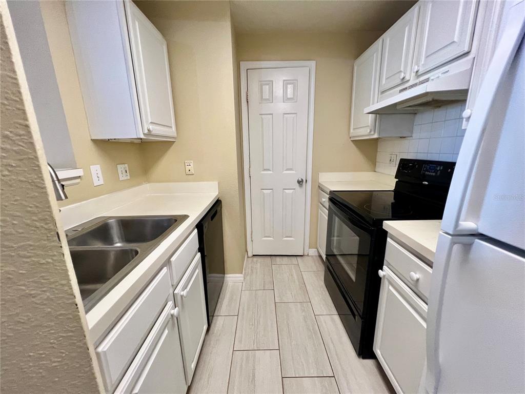 A galley kitchen features white cabinets, black appliances, and light-colored tile flooring — 501 KNIGHTS RUN AVENUE UNIT 1330, TAMPA, FL