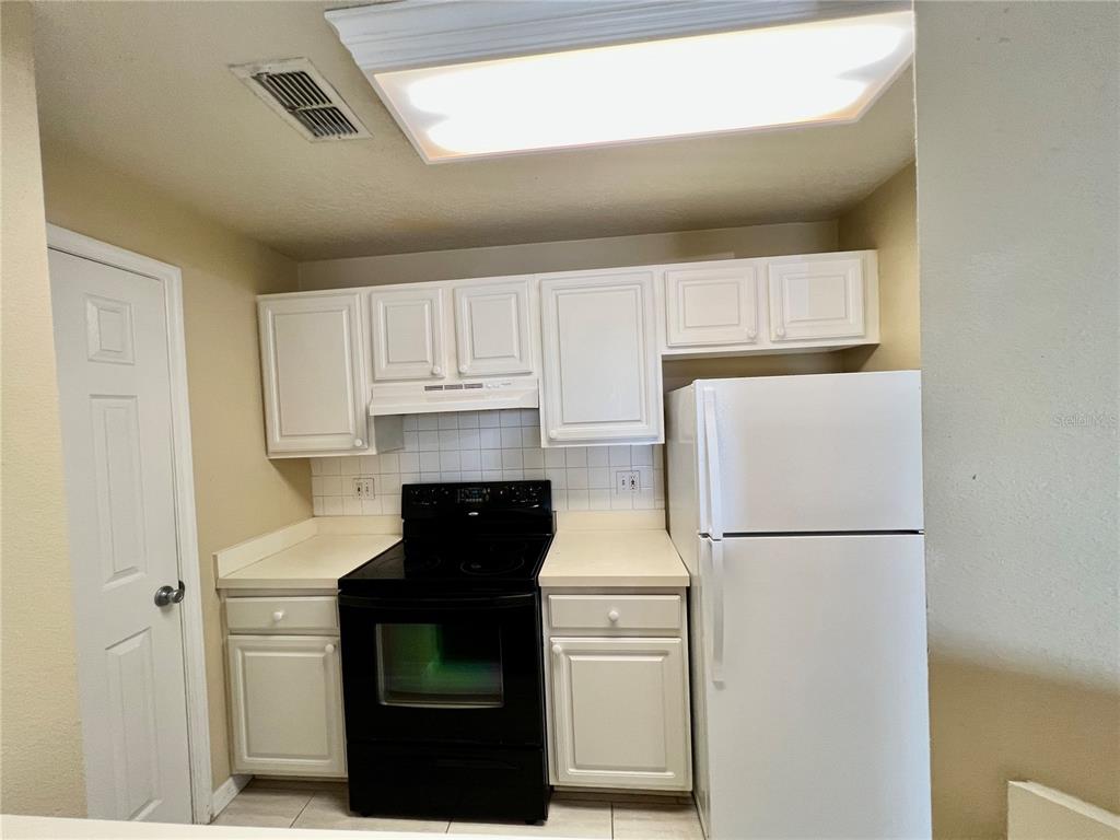 A kitchen features white cabinets, a black electric stove, and a white refrigerator — 501 KNIGHTS RUN AVENUE UNIT 1330, TAMPA, FL
