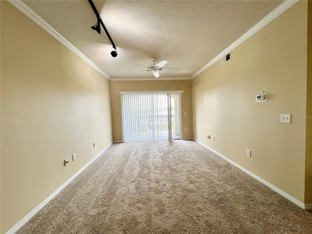 An empty living room features beige walls, tan carpeting, a ceiling fan, and sliding glass doors — 501 KNIGHTS RUN AVENUE UNIT 1330, TAMPA, FL