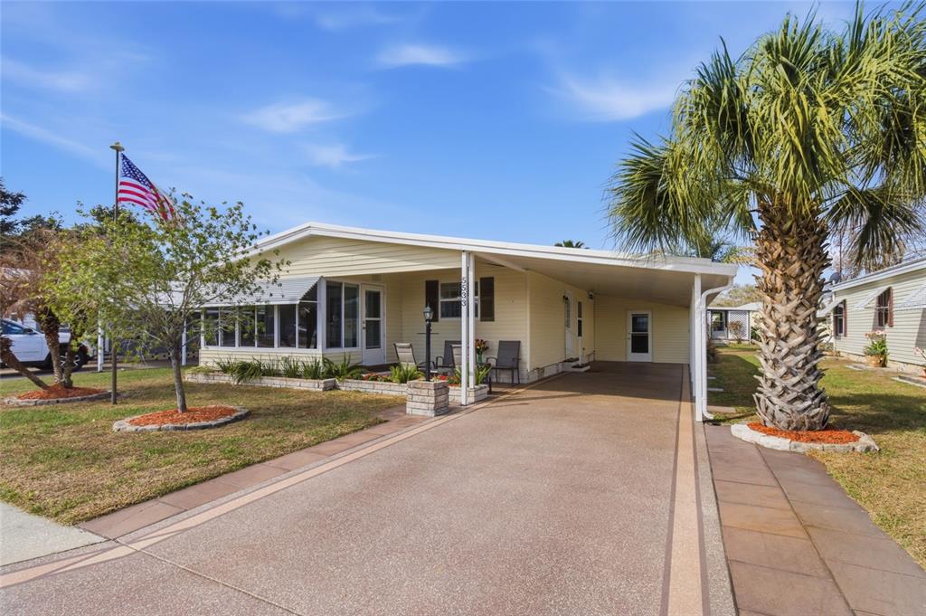 A yellow single-story mobile home features a carport, a screened porch, and a palm tree — 5533 REGAL WAY, ZEPHYRHILLS, FL