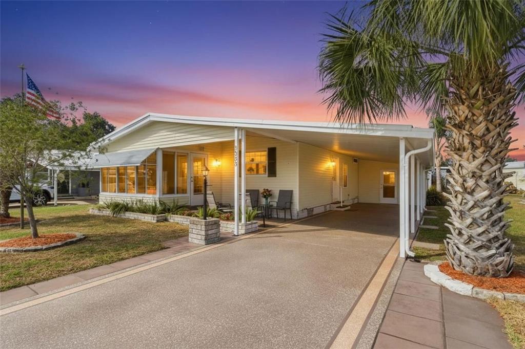 A light yellow manufactured home features a covered carport, front porch, and a palm tree — 5533 REGAL WAY, ZEPHYRHILLS, FL