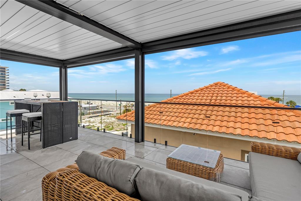 A covered balcony features outdoor furniture, a glass railing, and a view of the ocean — 30 80TH AVENUE, TREASURE ISLAND, FL
