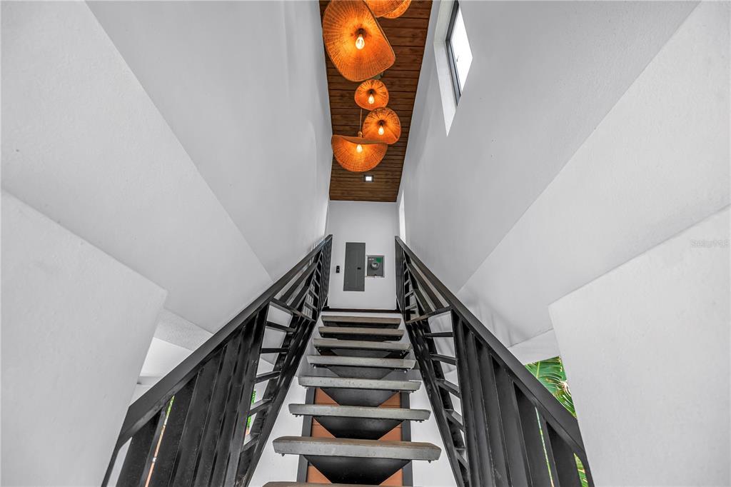 A staircase with black railings leads upward toward a ceiling featuring several hanging woven lights — 30 80TH AVENUE, TREASURE ISLAND, FL